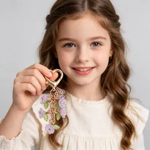 Detail of purple flower keychain with gold heart clasp and butterfly charms held by a girl
