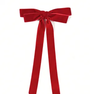 Detail of red velvet bow hair clip showing premium texture and long ribbon design