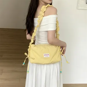 Detail of yellow nylon crossbody bag with ruffled shoulder straps and side drawstring bows