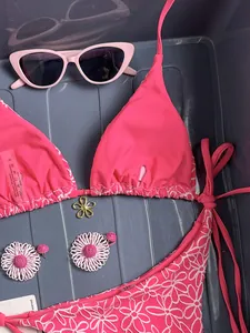 Detailed flat lay of pink daisy embroidered bikini with floral pendant and wash care label