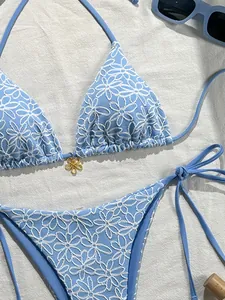 Detail of light blue bikini with white floral embroidery and gold flower pendant