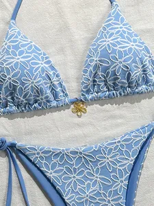 Detail of light blue bikini featuring white floral embroidery and gold flower pendant