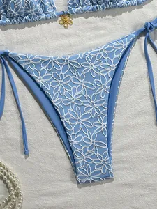 Detail of light blue bikini with white floral embroidery and gold flower pendant