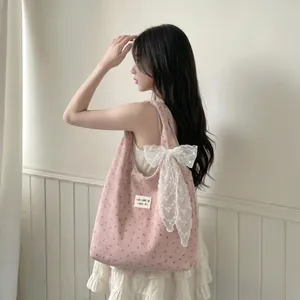 Gros plan du sac en velours rose à fleurs avec un grand nœud en dentelle blanche