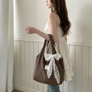 Détail du sac cabas en velours marron avec imprimé floral et nœud en dentelle blanche