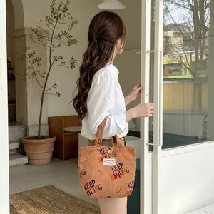 Detailed close-up of brown corduroy handbag with colorful Keep Smiling embroidery