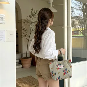 Detail of grey corduroy tote bag with Keep Smiling print held by a model in a cafe