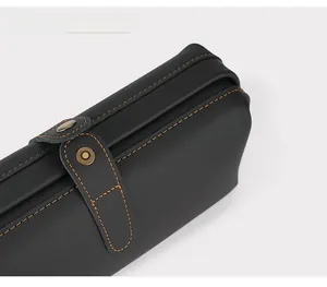 Detail of black leather bag showing orange contrast stitching and bronze metal button