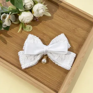 Close-up of white lace and satin bow hair clip with a round pearl pendant detail