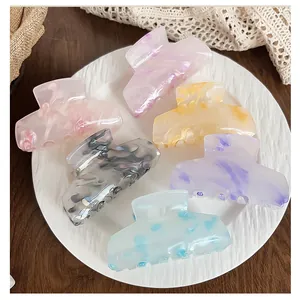 Close-up of six colorful marble-patterned acrylic hair claws on a ceramic plate