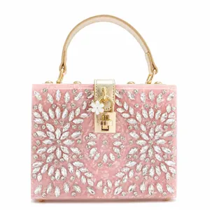 Macro detail of pink acrylic clutch bag with floral rhinestone patterns and gold handle