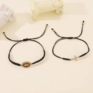 Detail of woven rope bracelets with gold cross and Virgin Mary charms on stone decor