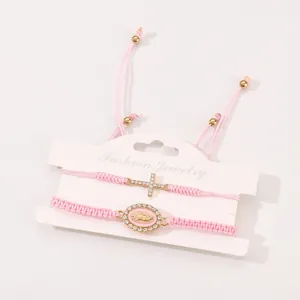 Detail of pink woven bracelets with gold cross and Virgin Mary charms on card
