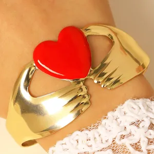Primer plano de brazalete dorado con dos manos sosteniendo un corazón rojo y encaje