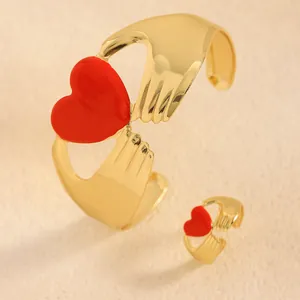 Detalle del conjunto de brazalete y anillo dorados con diseño de corazón rojo