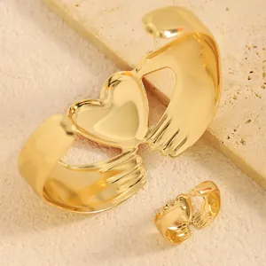 Detalle de conjunto de brazalete y anillo dorados con diseño de manos y corazón