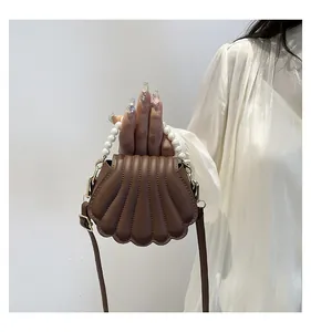 Détail d'un sac marron en forme de coquillage avec poignée perles et texture matelassée