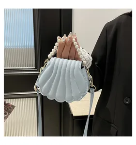 Sac à main bleu clair en forme de coquillage avec poignée en perles porté par un mannequin