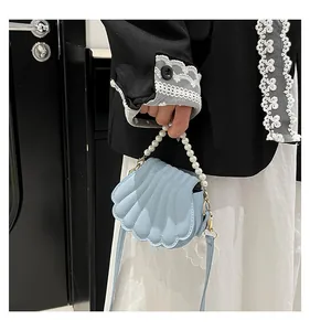 Vue détaillée du sac en forme de coquillage bleu clair avec anse en perles et cuir plissé