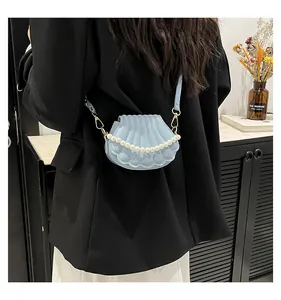 Détail du sac coquillage bleu clair avec anse en perles porté par un mannequin en costume