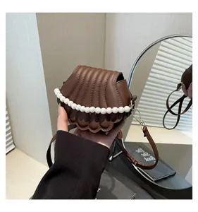 Détail d'un sac à main marron en forme de coquillage avec textures 3D et perles blanches