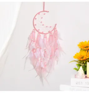Detail of pink moon-shaped dreamcatcher with feathers and pearls on white wall