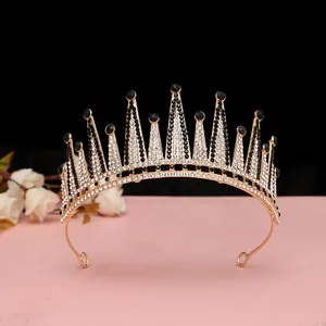 Dettaglio corona dorata con cristalli bianchi e neri su superficie rosa chiaro