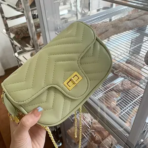 Detail of light green quilted crossbody bag with golden hardware and V-shaped stitching