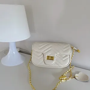 Detail of cream quilted crossbody bag with golden twist lock and heart pendant