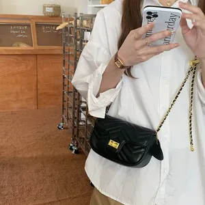 Detail of a black quilted crossbody bag with golden clasp and leather chain strap