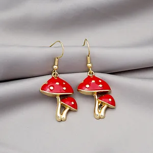 Charming red mushroom earrings with gold spots on a soft grey textured fabric
