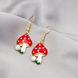 Close-up of red and white mushroom drop earrings with gold hooks and tiny pearl detail
