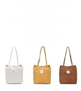 Detailed close-up of corduroy tote bags in white, yellow, and brown with leaf patch