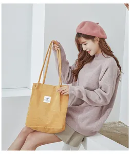 Detail of yellow corduroy tote bag featuring a minimalist white label and long shoulder straps