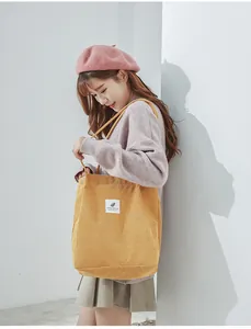 Detail view of yellow corduroy tote bag showing textured fabric and brand patch