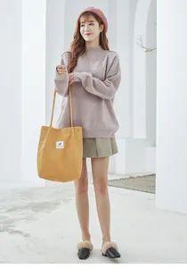 Detail of a ginger yellow corduroy tote bag with white label and metal buckle accessory