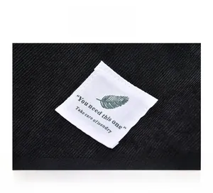Macro shot of white embroidered tag with green leaf and text on black corduroy bag