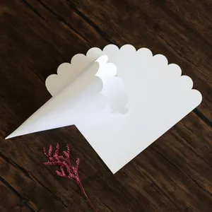 White scalloped edge paper confetti cone for weddings displayed on a wooden surface