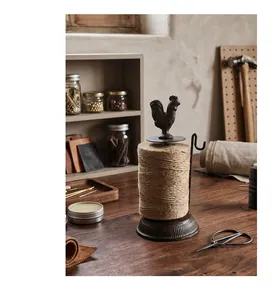 Rustic cast iron rooster twine dispenser with jute rope shown on a vintage workbench