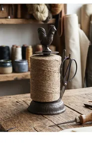 Detail of a vintage cast iron rooster twine holder with scissors on a rustic wooden table.