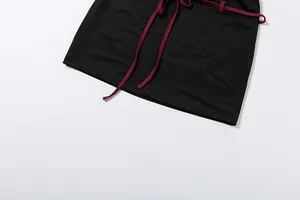 Détail d'une mini-jupe moulante noire avec une ceinture à nouer bordeaux et l'ourlet.