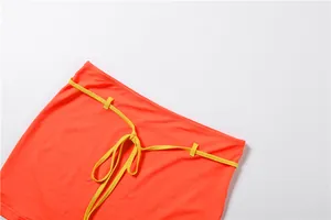 Vue détaillée d'une mini-jupe moulante orange sexy avec une ceinture jaune à nouer.