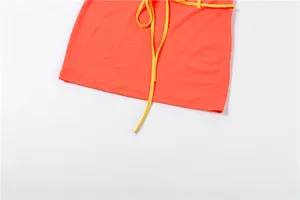 Détail d'une mini-jupe moulante orange vif avec une ceinture à nouer jaune éclatante.