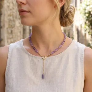 Elegant detail of a purple amethyst beaded necklace with gold clasp worn by a model.