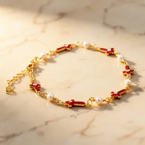 Detail showing red enamel cross charms and white pearls on a gold-plated link bracelet