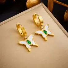Detail of gold butterfly drop earrings with white shell wings and a green gemstone