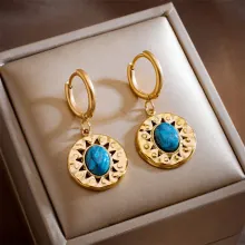 Close-up of gold drop earrings with blue stone inlay and sunburst engraving on box