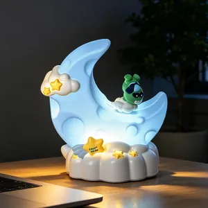 Luce notturna a luna cartoon con base a nuvola e personaggio verde su scrivania in legno
