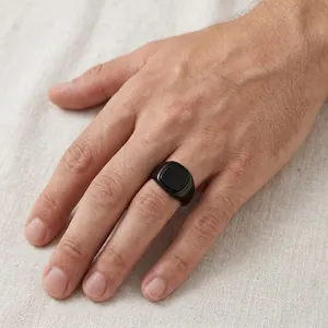 Detail shot of a minimalist men's square black signet ring worn on hand over linen