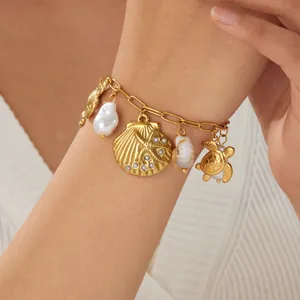 Detailed view of gold ocean charm bracelet with shell, turtle, and pearl on model.
